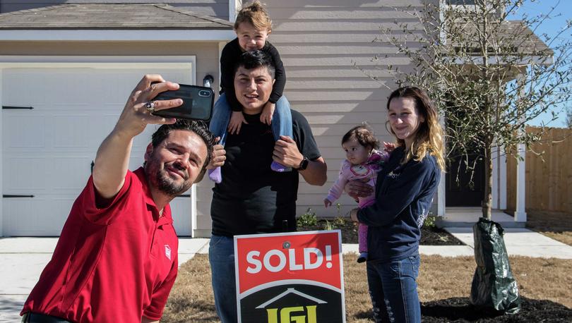 Sales Rep holding phone and taking photo of happy family in front of their new home.