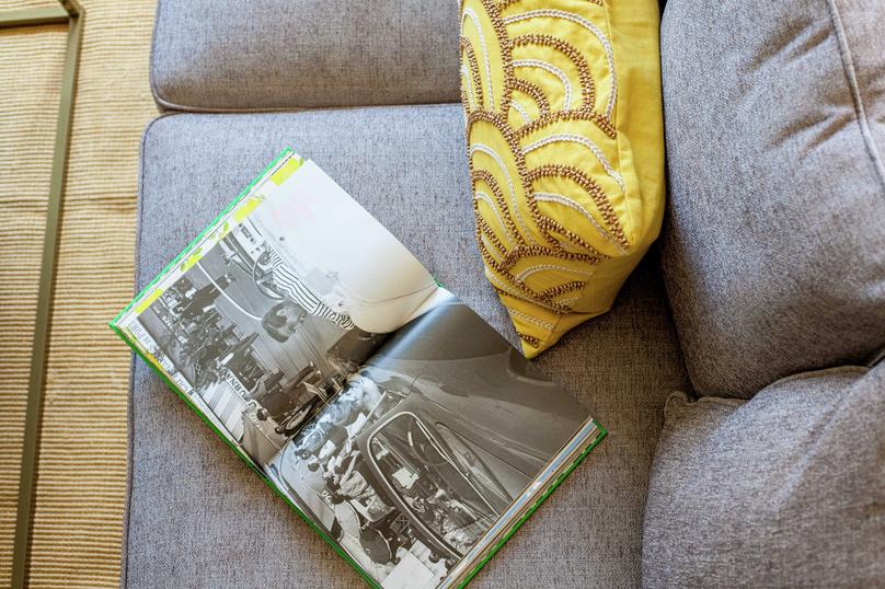 Staged living room with grey sofa, yellow throw pillow with brown pattern, and open book with black and white picture on it
