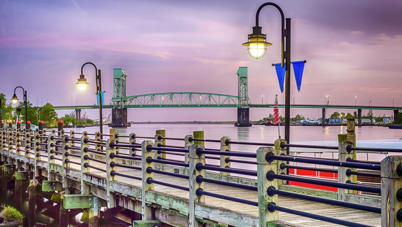 Wilmington, North Carolina Riverwalk at night time with lit pier, algae on the wood, and bridge in the background