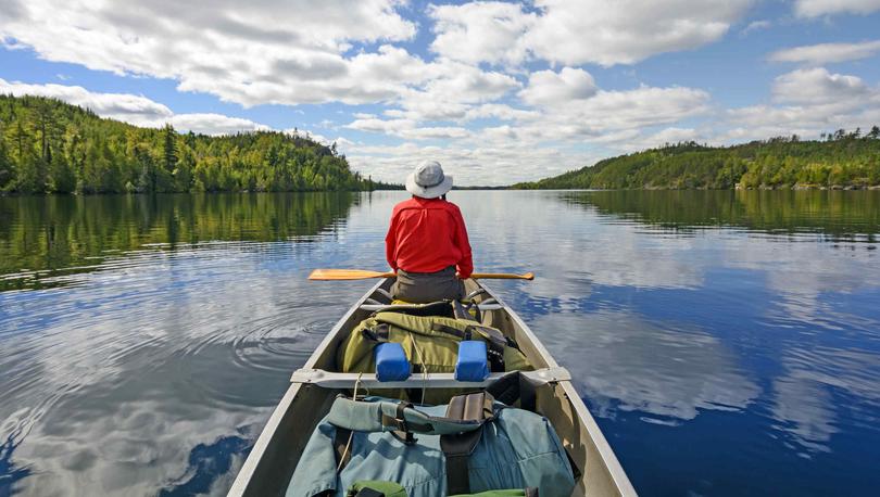 Person canoeing on serene lake surrounded by trees