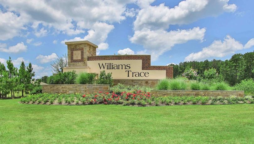 Williams Trace entrance monument with green grass, red flowers, pine trees in background.