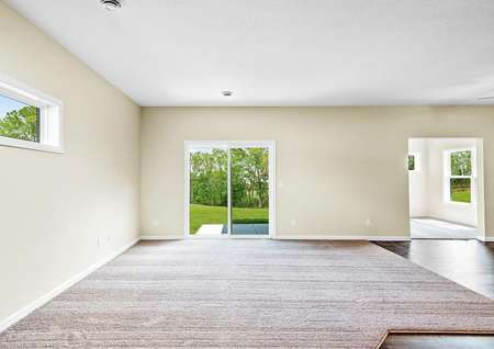 Photo of a carpeted living room with a sliding glass door and adjacent dining room with plank flooring and view into 4-season porch.