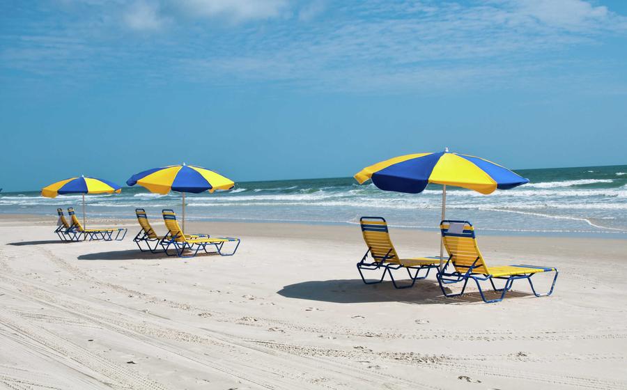 Daytona Beach, Florida beach with blue and yellow sunshades with loungers, white sands, and rolling tides