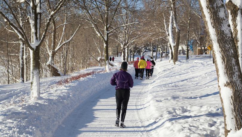 Minneapolis, Minnesota snow-covered park with joggers on the trail, leafless trees, and blue skies