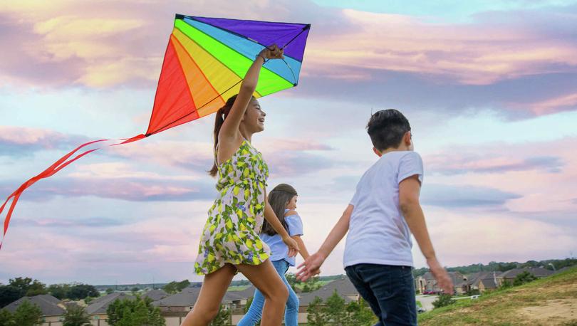 Three kids running with a kite in a park.