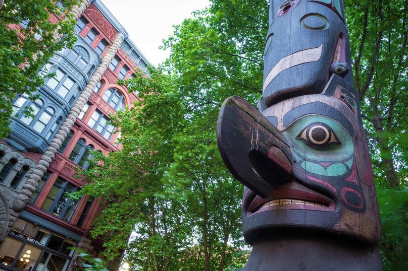 Totem pole at Pioneer Square in Seattle, WA with the Pioneer Building in the background, which was originally constructed in 1892
