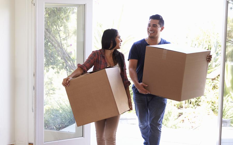 A young couple carries moving boxes into their new home.