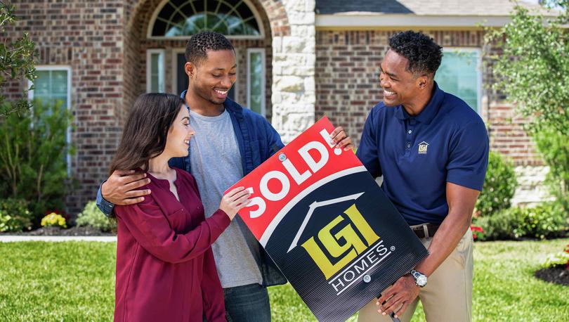 Couple with a sold sign in front of their new home.