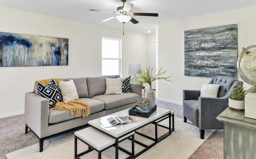 A fully furnished living room that has a ceiling fan, white walls and light-brown carpet flooring