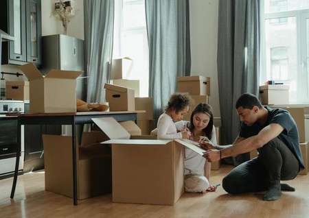 A young family sits on the floor drawing on a box and is surrounded by moving boxes.