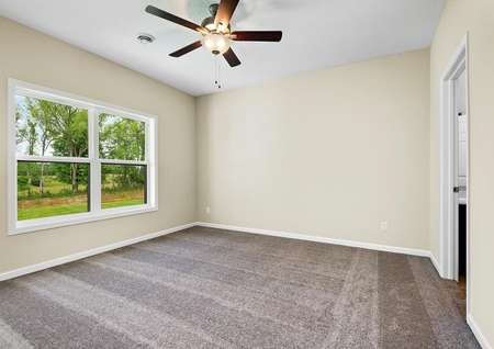 Photo of the primary bedroom with carpet, a ceiling fan and a large window overlooking the back yard.