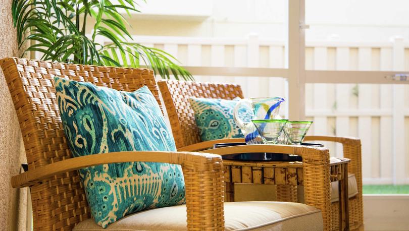 Sea Forest Beach Club model home completed with wooden chairs that have turquoise pattern pillows and beige cushions, table with glasses sitting on it, and a house plants in the background