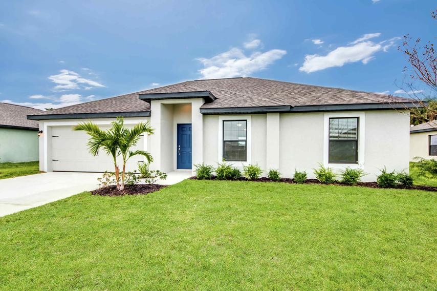 Side and front view of the Vero floor plans model home with a front yard that has lush green grass, plants and a small tree in front of it.