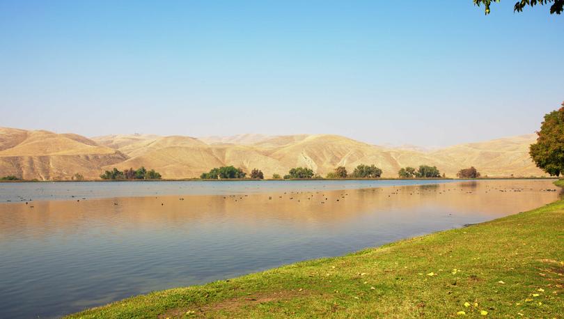 Bakersfield, California Lake Ming man-made recreational area with calm waters, lined with green grass, and mountain ranges in the distance