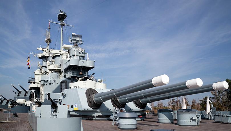 USS North Carolina warship with three large cannons, wooden deck, and machine guns